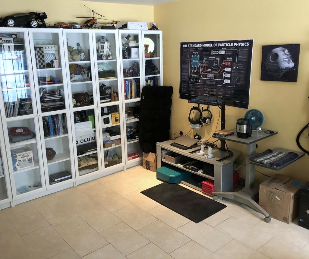 A mostly empty tile floor, a small amount of computer equipment up against one wall, the other wall an array of bookshelves.